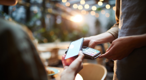 Close-up of unrecognizable woman using modern gadget while making online payment in cafe, nfc technology concept